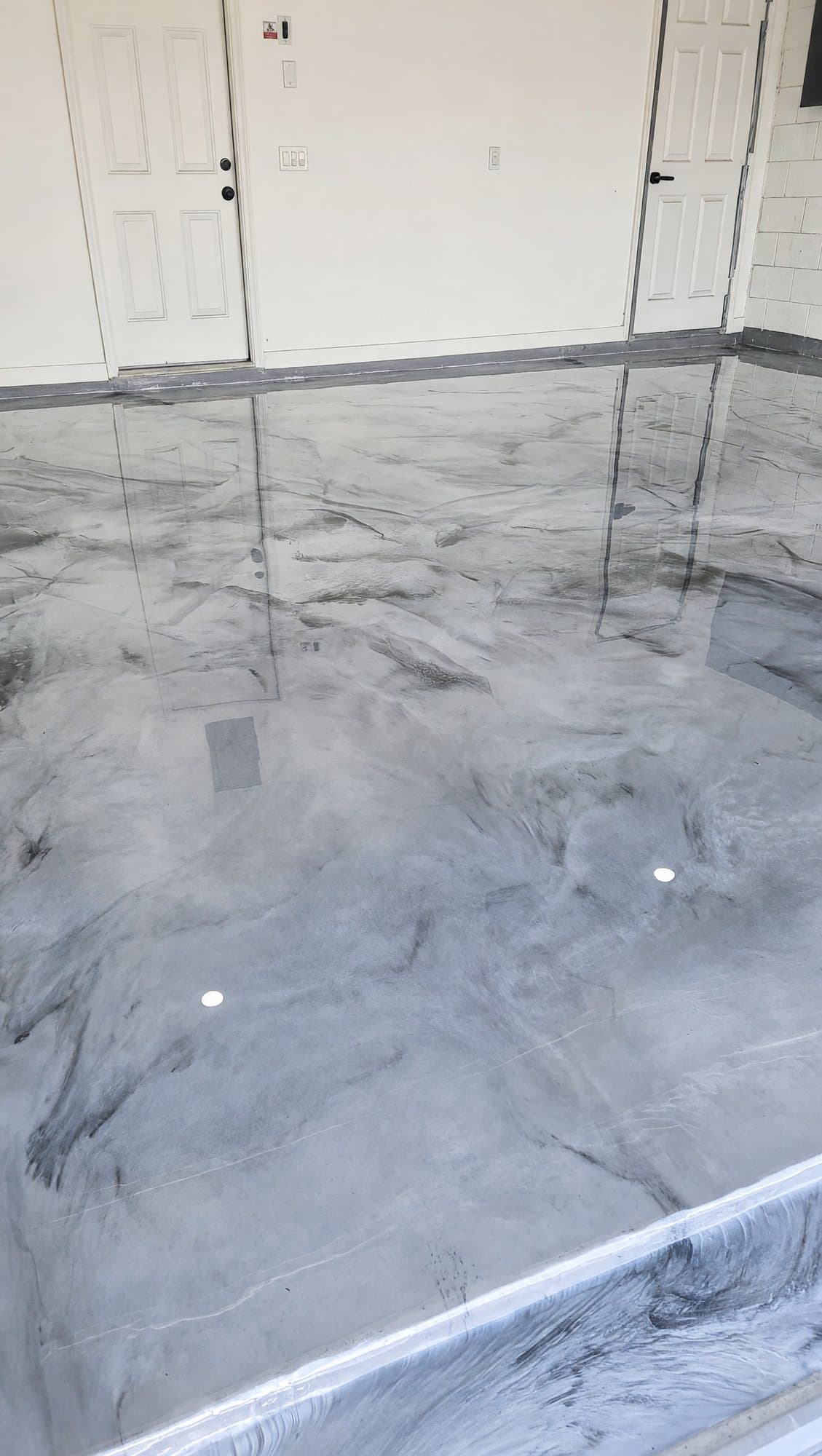 High-gloss gray and white metallic epoxy floor in a residential garage, reflecting white doors