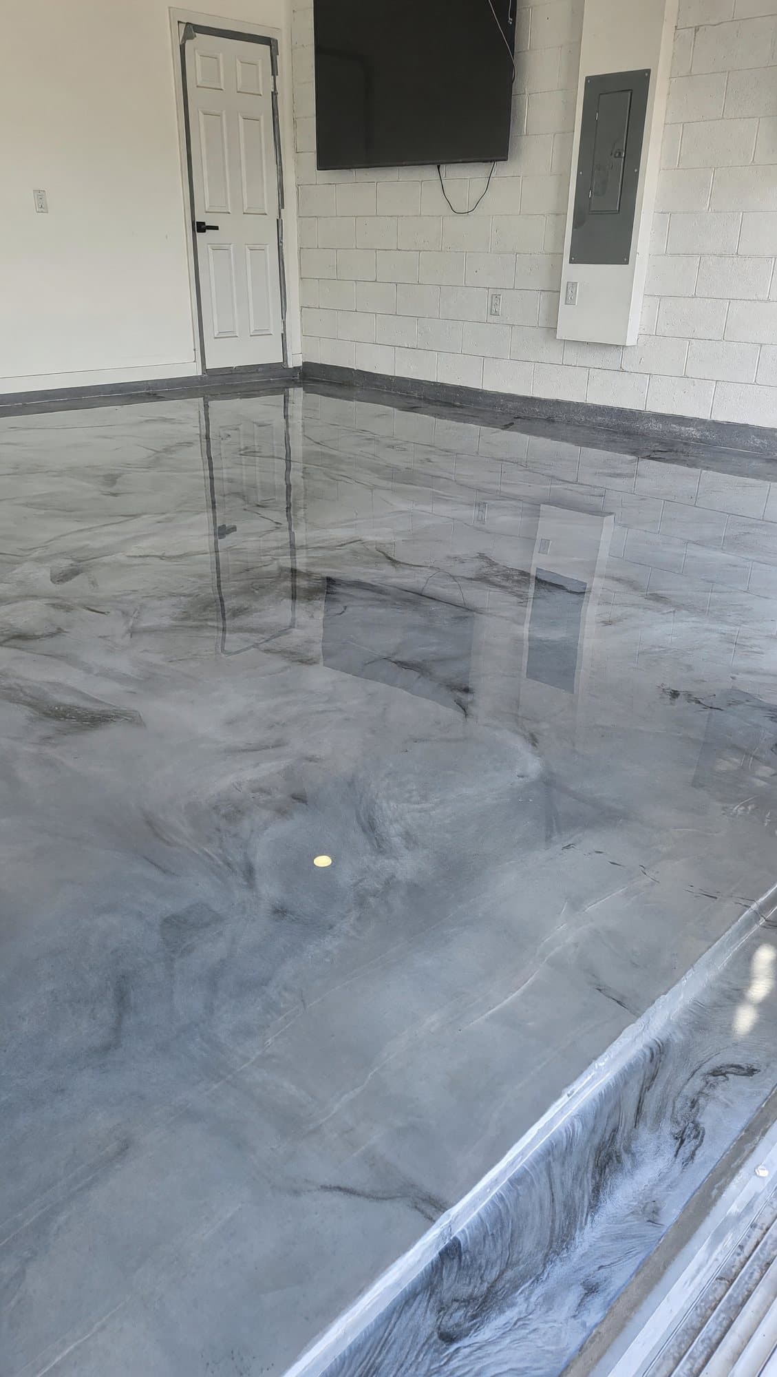 High-gloss gray and white metallic epoxy floor in a residential garage with a painted block wall