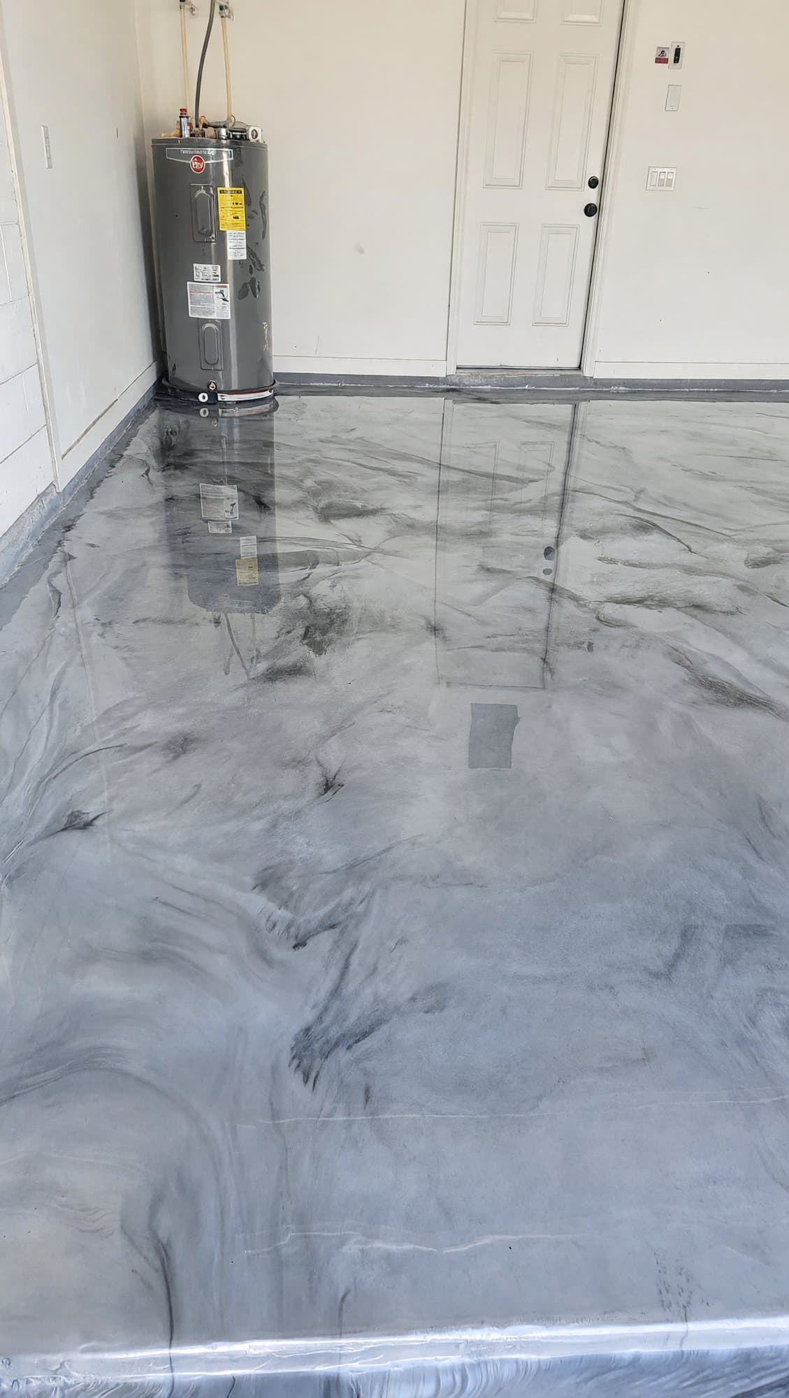 High-gloss gray and white metallic epoxy floor in a residential garage beside the water heater